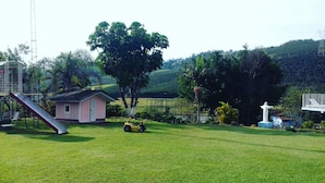 A grassy field with a small pink building, a slide, and a yellow toy car.