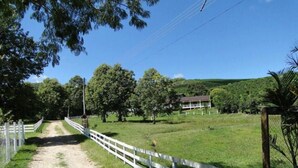 A rural road leading to a house surrounded by trees and a fenced field. - Pousada Sitio Bom Fim (Serra Negra)
