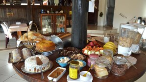 A buffet table with various food items including bread, cakes, fruits, and condiments. - Pousada Sitio Bom Fim (Serra Negra)