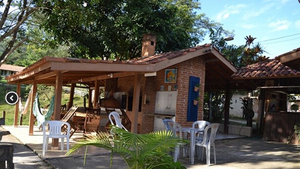 A rustic outdoor seating area with a brick building, a covered patio, and a small garden. - Pousada Sitio Bom Fim (Serra Negra)