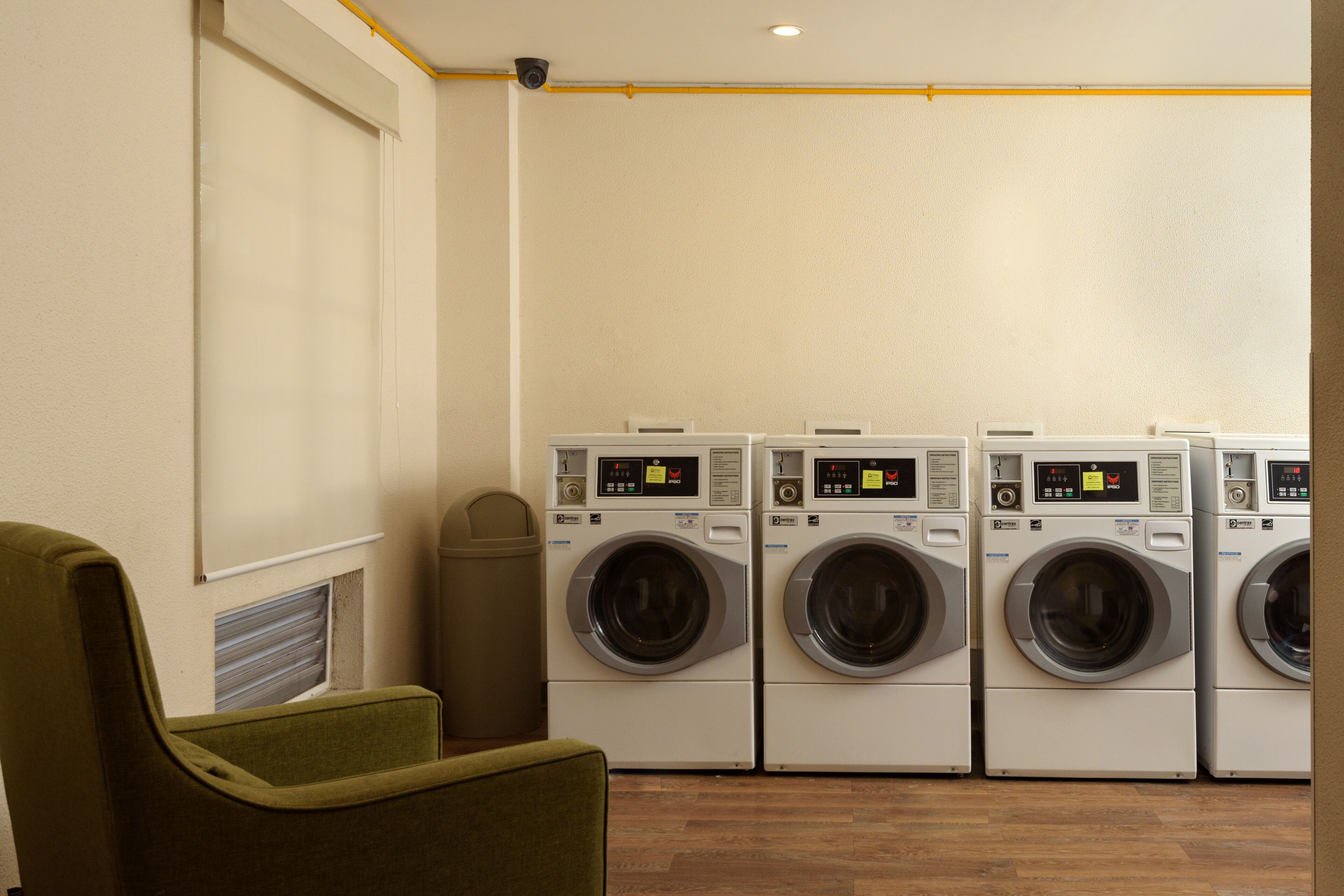 A laundry room with four front-loading washing machines and a single chair.