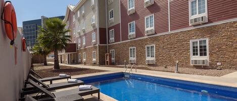 Una piscina al aire libre, sombrillas, sillones reclinables de piscina