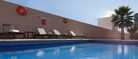 Una piscina con sillas de descanso y flotadores en la pared.