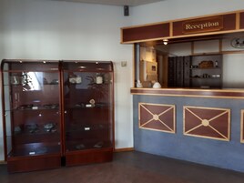 Bancada de recepção com placa indicando 'Reception', uma vitrine de vidro com sapatos, e uma parede azul com padrões geométricos.