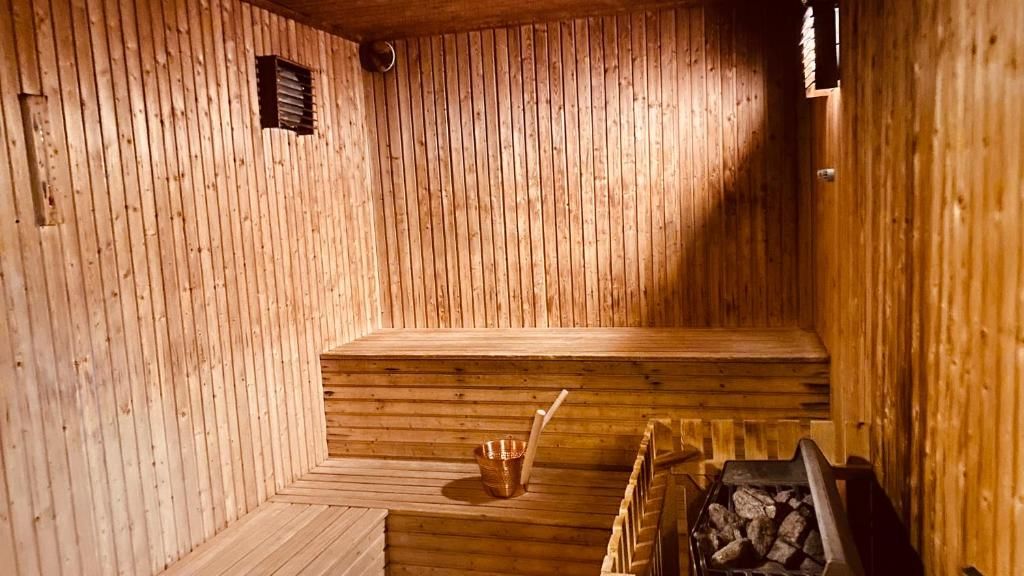 Una sauna con paredes y bancos de madera, un balde pequeño y un estufa de leña.