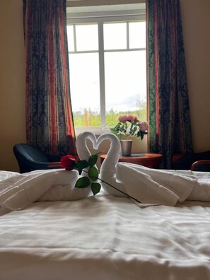 A bed with a white duvet, a single rose, and two swans made of fabric. - Hotell Indalsleden (Bispgården)