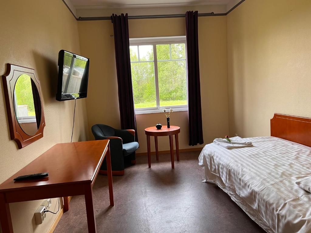 A hotel room with a bed, a desk, a chair, a TV, and a window with curtains.