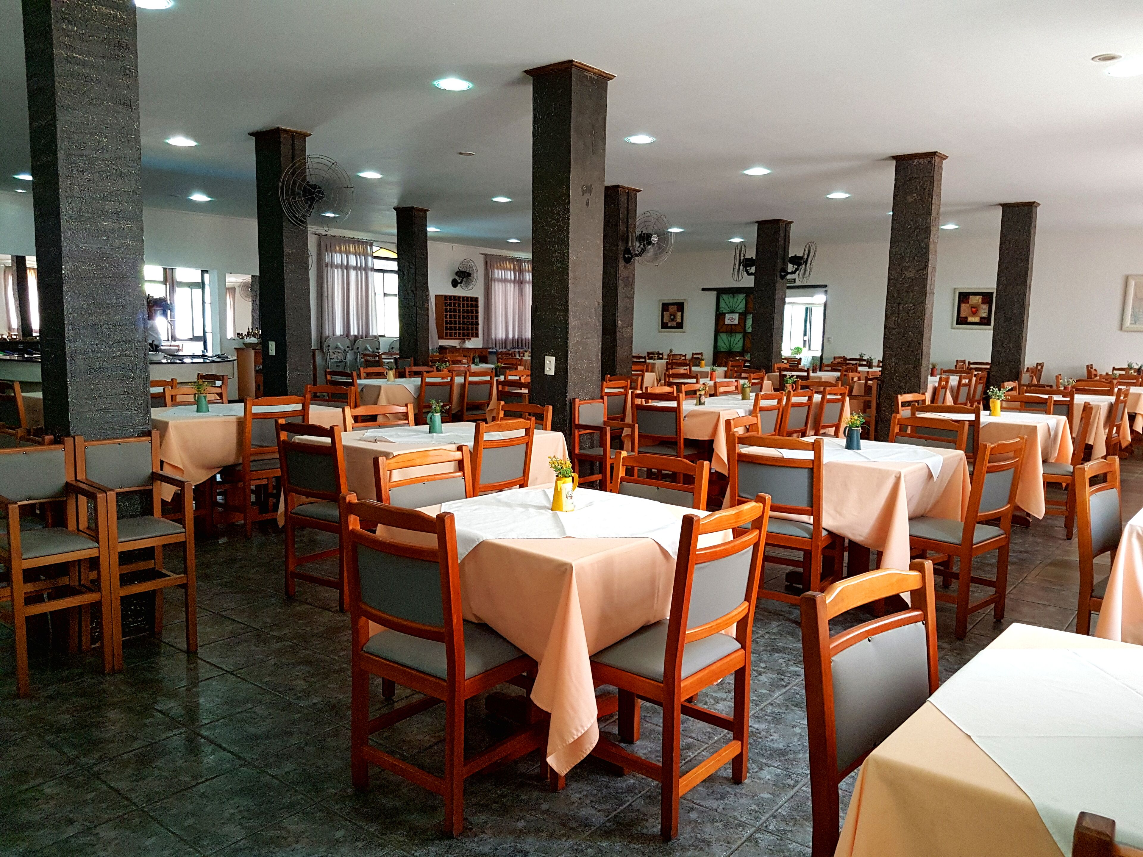 A spacious dining area with multiple tables and chairs, large pillars, and ceiling lights.