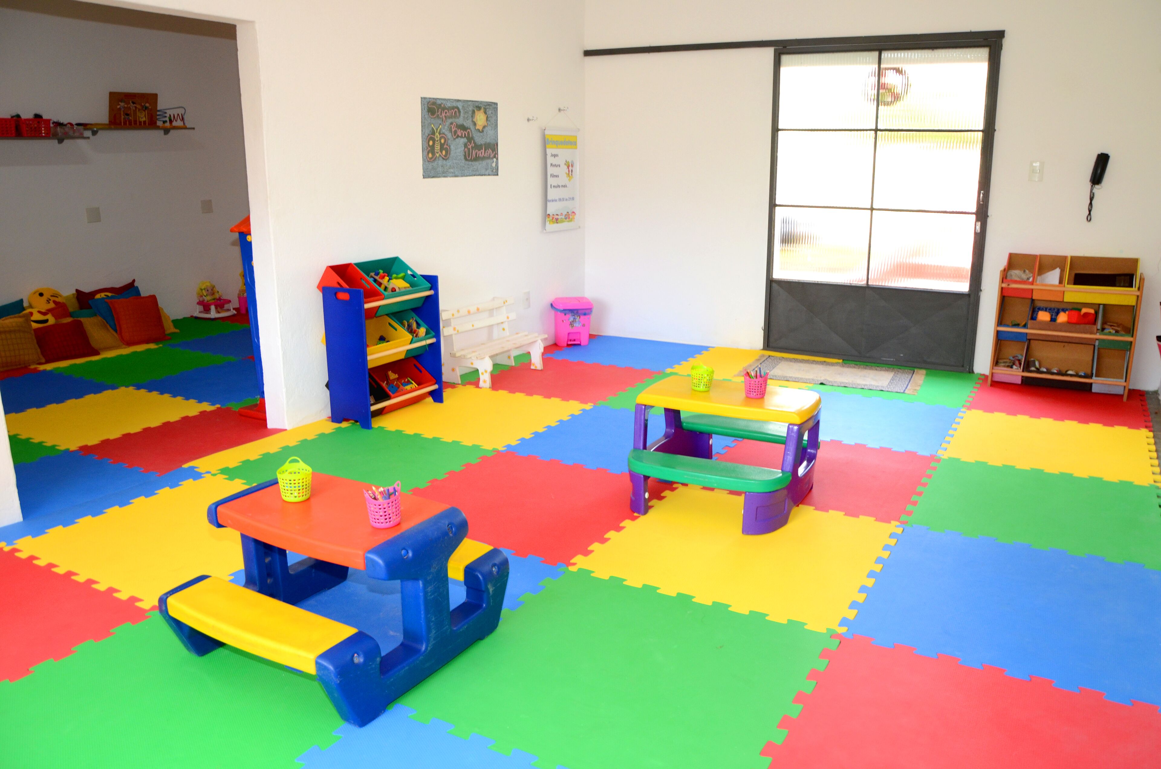 Una sala de juegos con alfombras de espuma de colores, mesas y sillas.