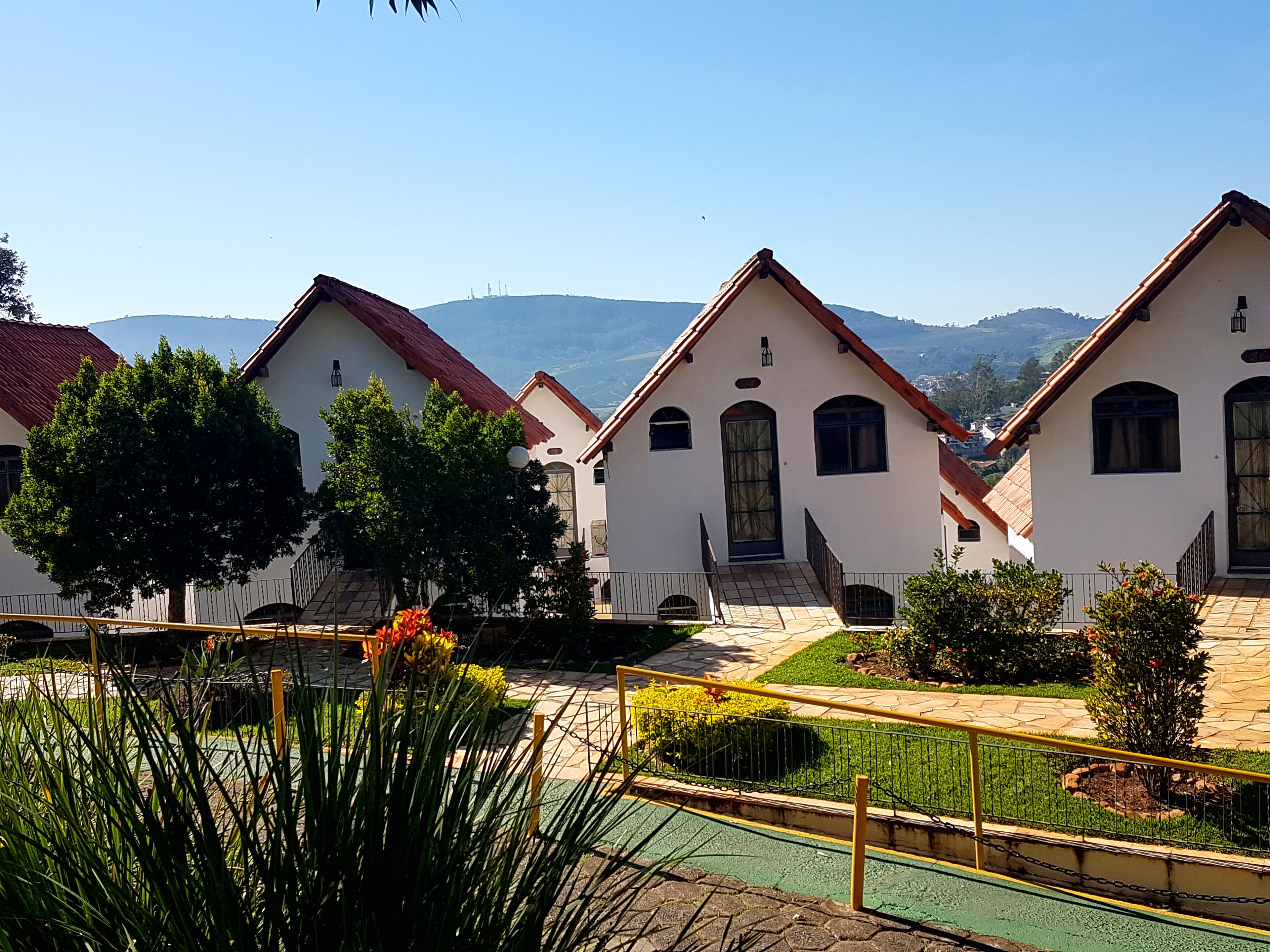 A row of white buildings with red roofs, surrounded by greenery and a clear sky.