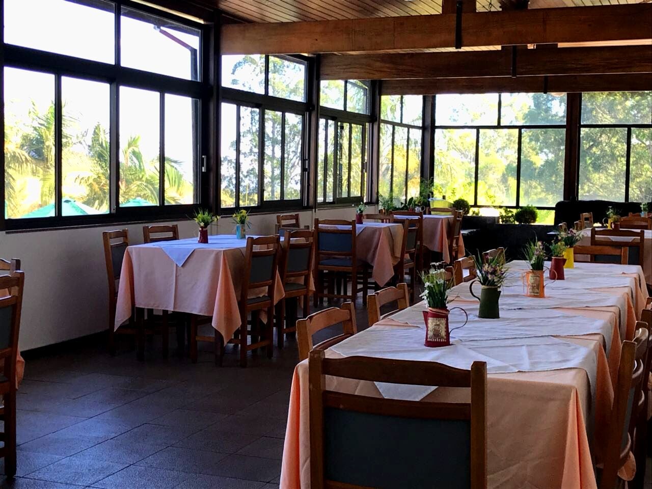 A dining area with tables set for guests, large windows with a view of palm trees, and wooden chairs.