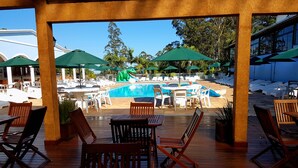 Un área junto a la piscina con sillones de madera, una piscina y sombrillas.