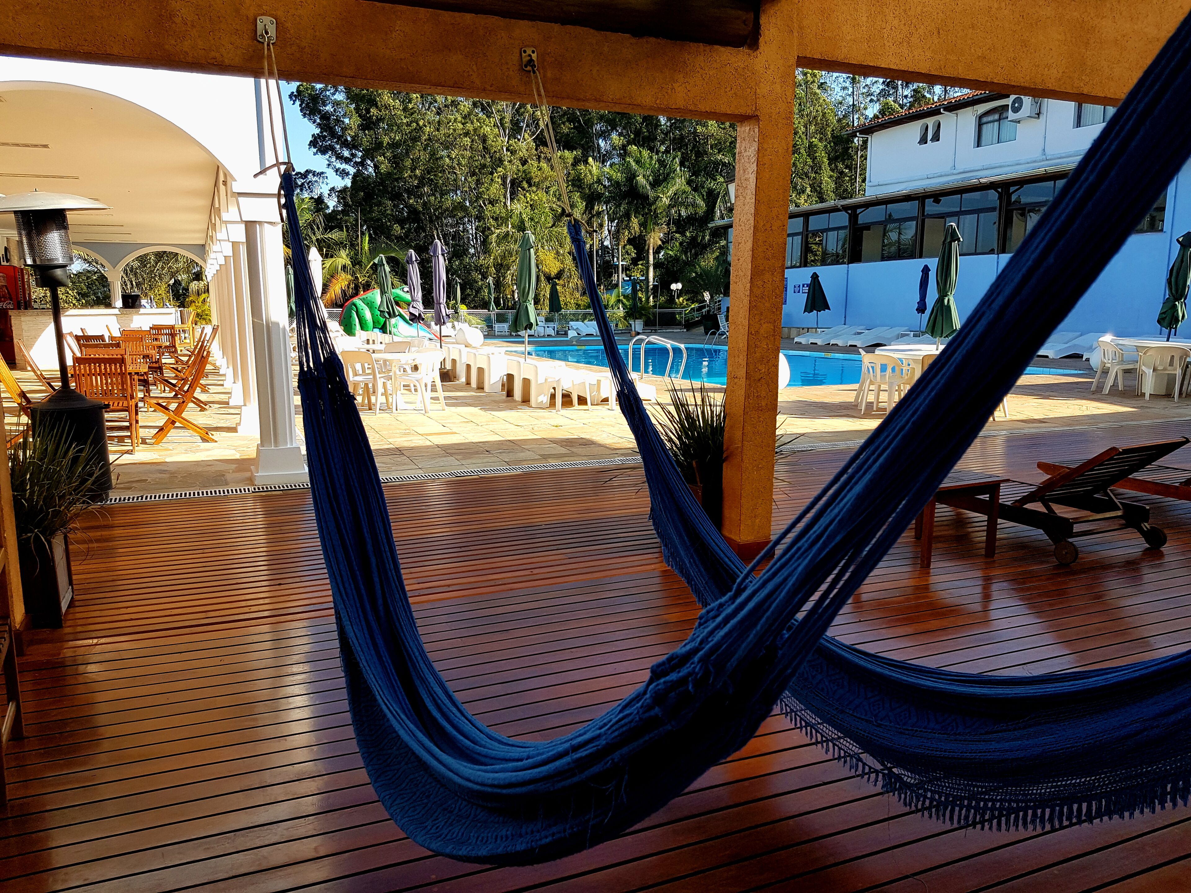 Uma rede em um deck de madeira com vista para uma área de piscina, com cadeiras de sol e guarda-sóis.