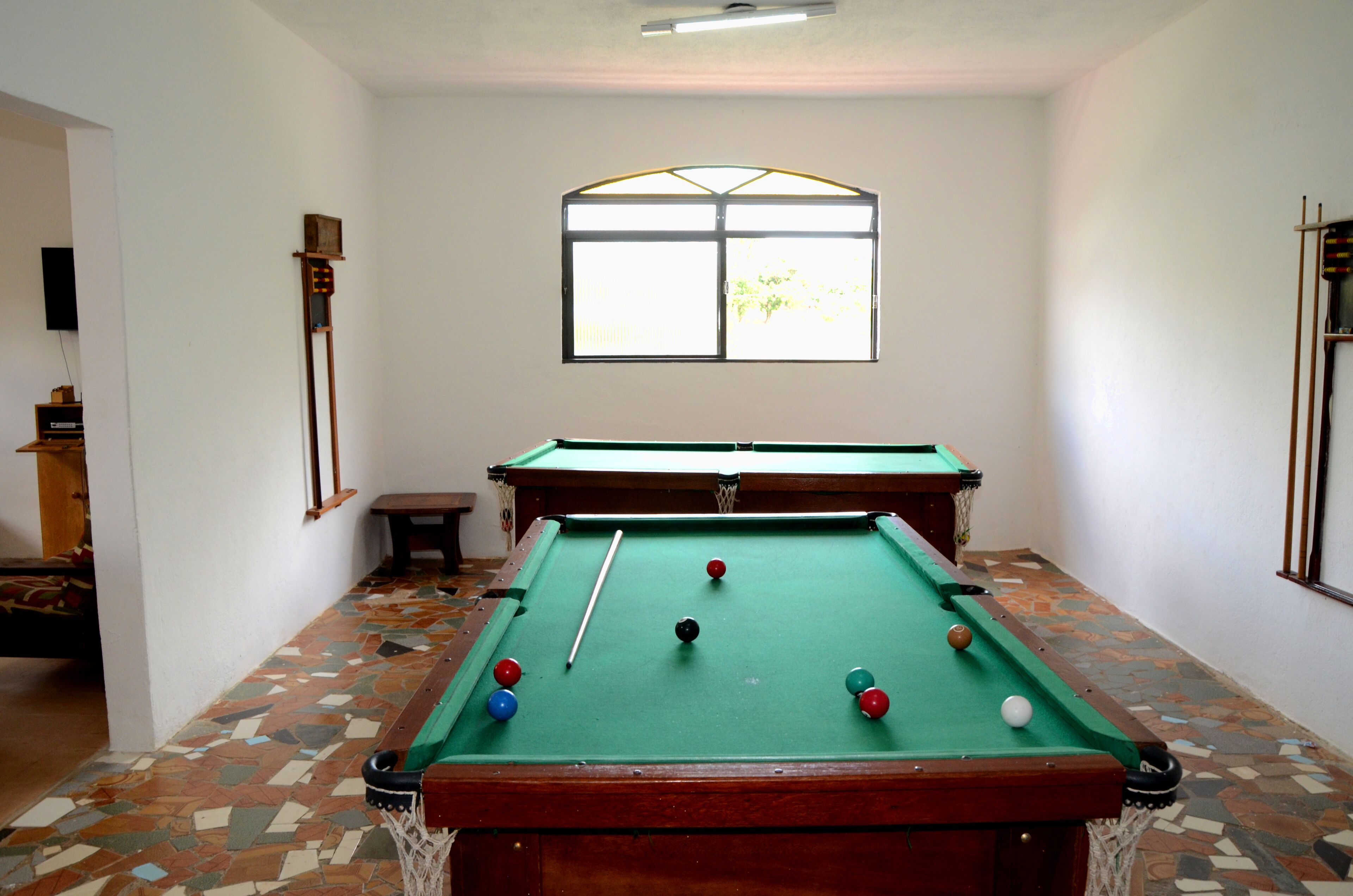 A pool table with balls and a cue stick, a window, and a tiled floor.