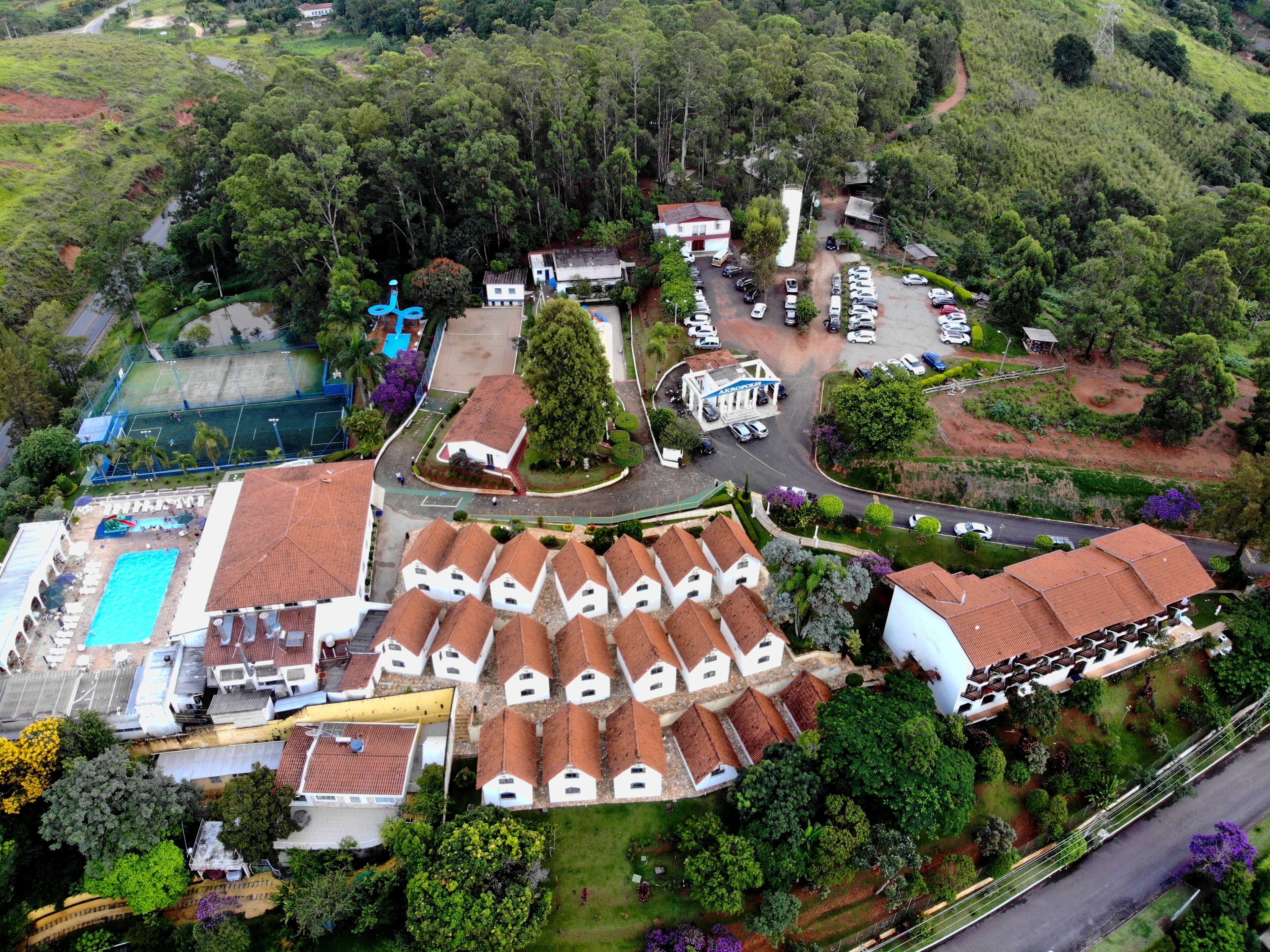 An aerial view of a resort with multiple bungalow-style buildings, a swimming pool, and a tennis court.