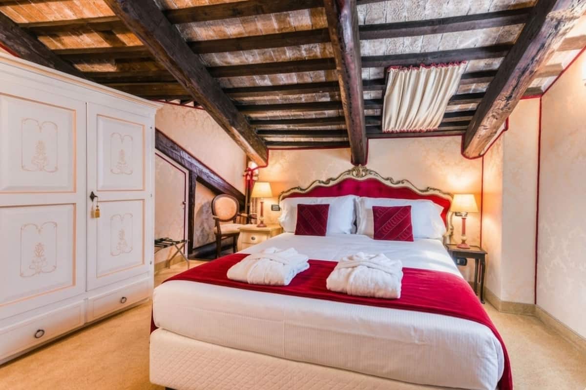Un dormitorio con una cama grande, techo de madera, armario y mesita de noche con lámpara.