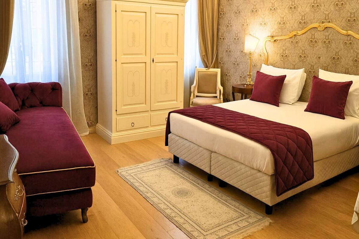 Un dormitorio con cama, mesita de noche, silla, armario y ventana con cortinas.
