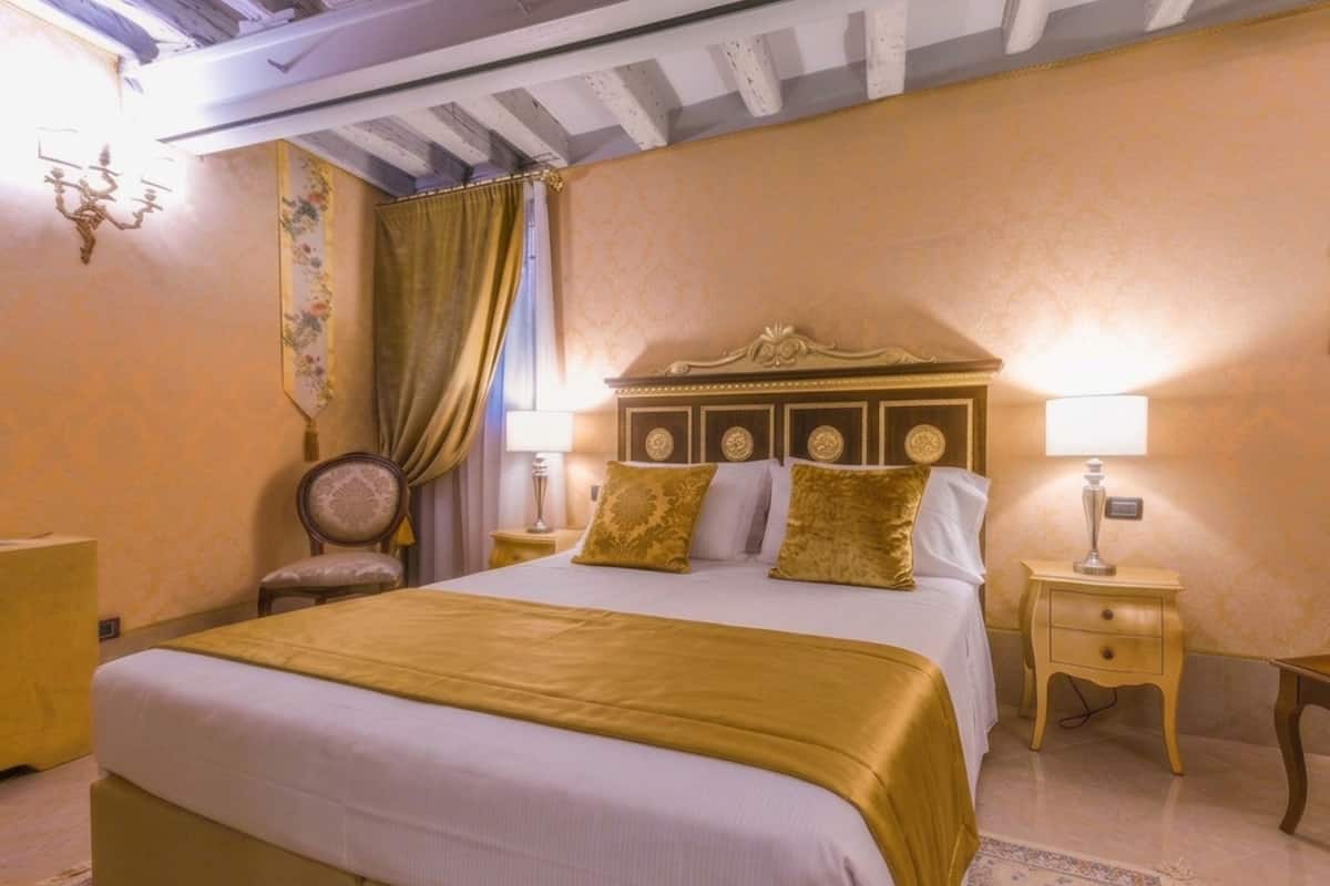 Habitación de hotel con una cama grande, dos mesitas de noche, una silla, una araña y un adorno en la pared.