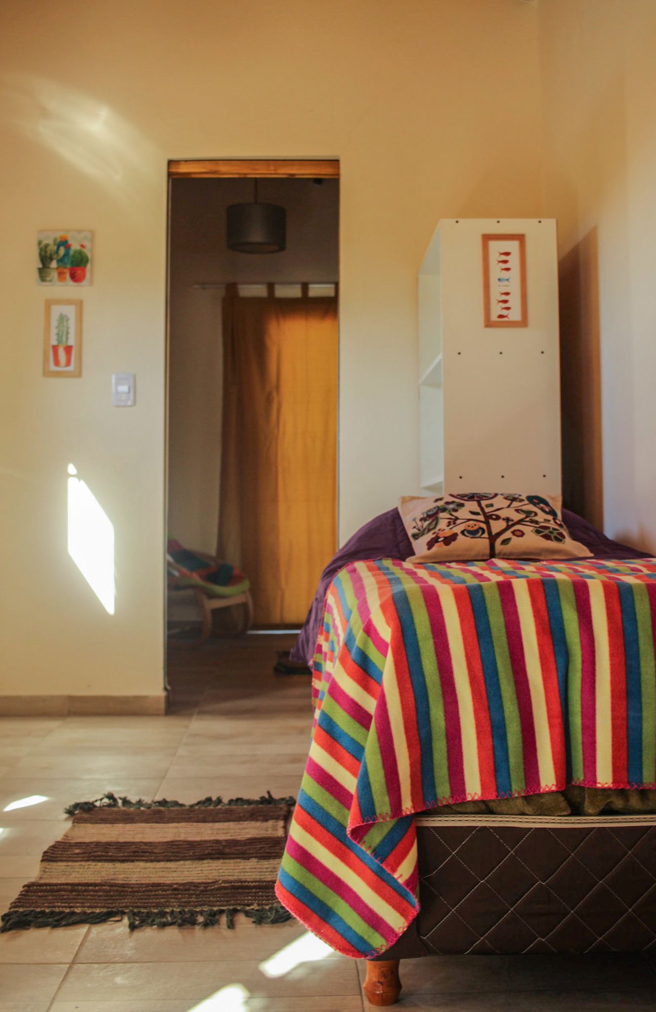 A bedroom with a striped bedspread, a wooden headboard, a small rug, and a door leading to another room.