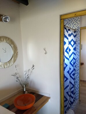 A bathroom with a wooden vanity, an orange bowl sink, a mirror, and a shower with a patterned curtain. - Arriba del Valle - Casas de Altura (Potrerillos)