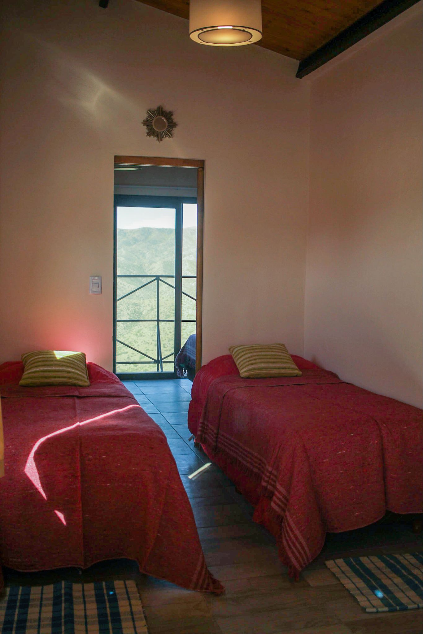 Une chambre avec deux lits, chacun recouvert d’une couverture rouge et doté d’un oreiller. Une grande fenêtre offre une vue sur l’extérieur.
