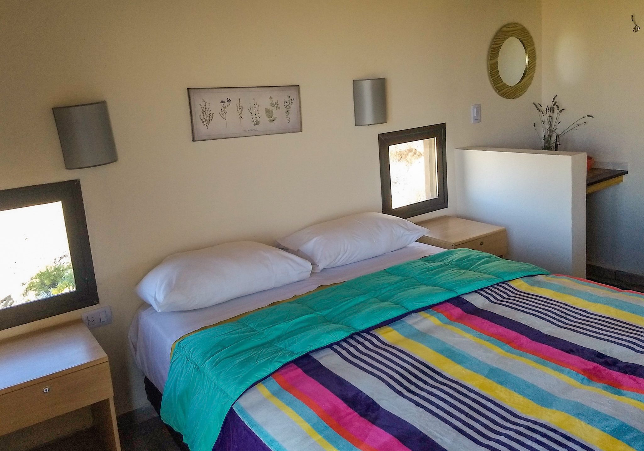A bedroom with a bed, a bedside table, a nightstand, a dresser, a mirror, and a wall-mounted picture.