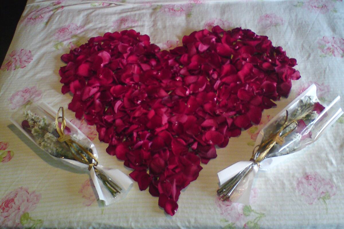 Ein Bett mit einer herzförmigen Anordnung aus Rosenblättern und zwei kleinen Blumensträußen.