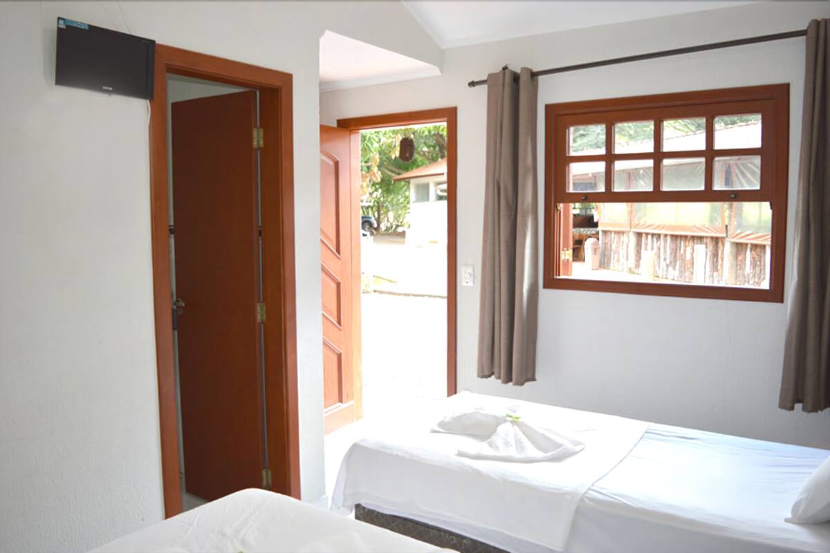Ein Hotelzimmer mit Bett, einem Fenster mit Vorhängen und einer offenen Tür, die nach draußen führt.