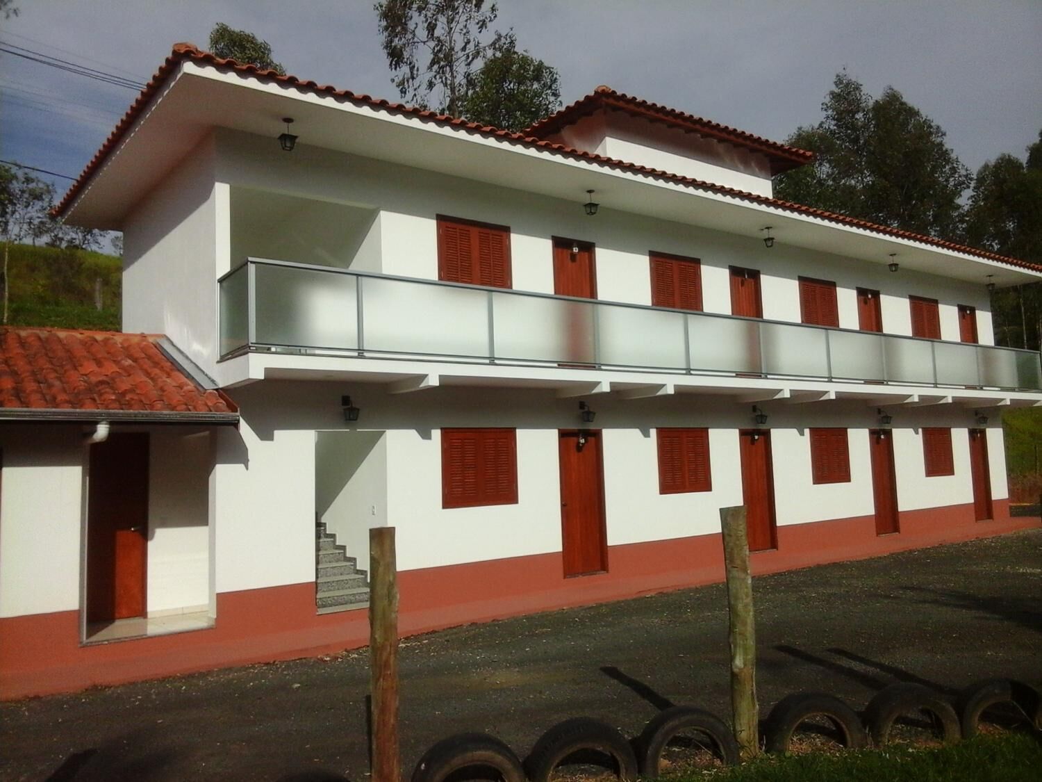 A two-story building with a white facade and red accents, featuring a balcony on the upper floor.