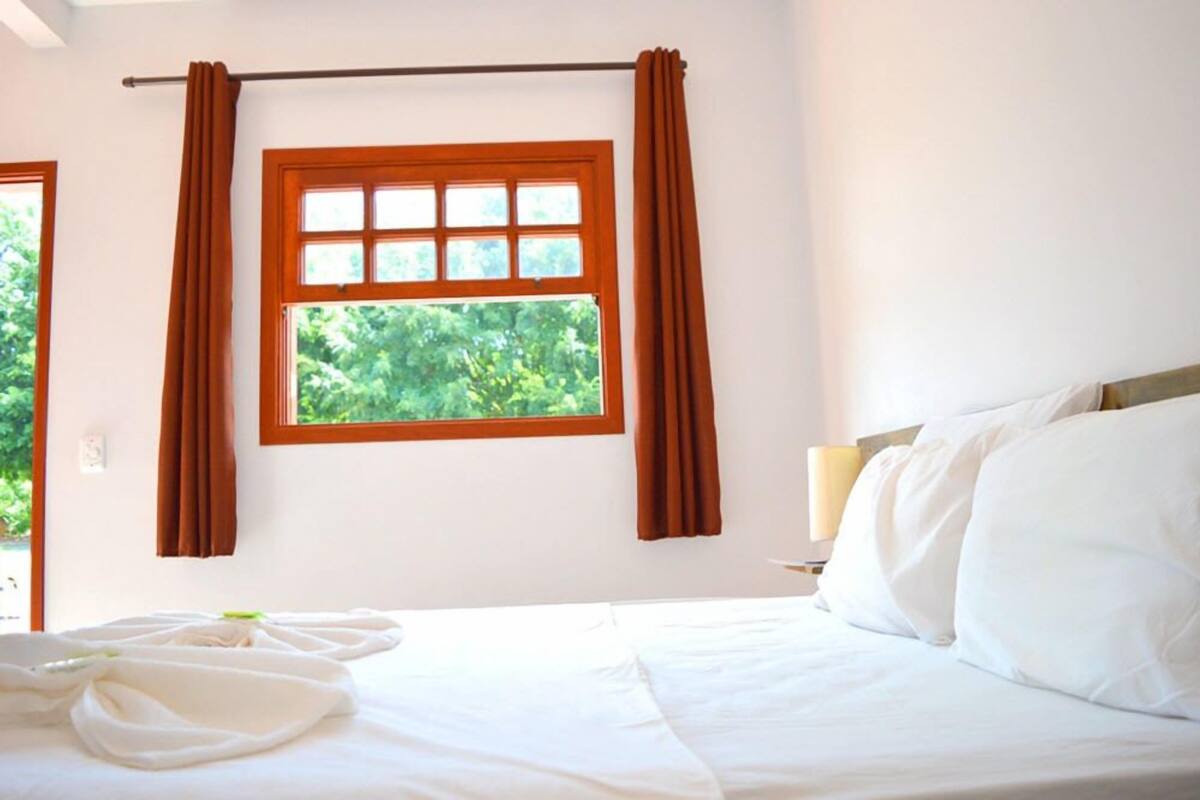 Ein Hotelzimmer mit Bett, einem fenster mit Vorhängen und Blick auf Grünfläche.