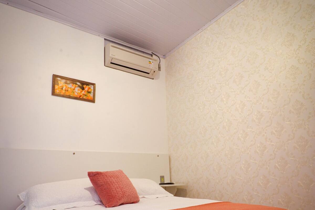 Une chambre à coucher comprenant un lit, une table de chevet, un appareil de climatisation et un tableau accroché au mur.