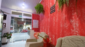 A reception area with a red wall, a signboard, a reception desk, and a seating area with a vase of flowers. - Pousada Tia Eni (Gramado)