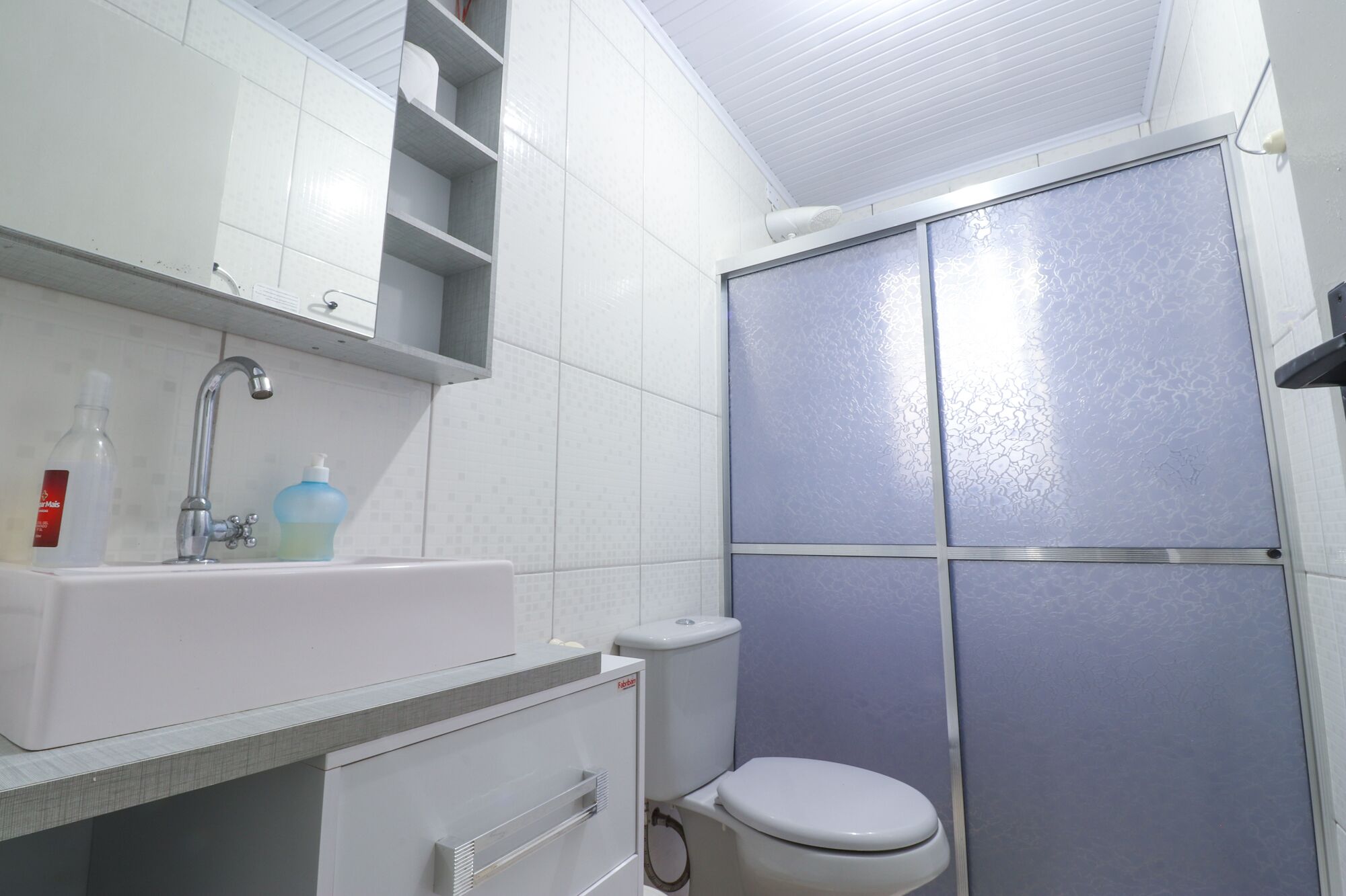 A bathroom with a white sink, two bottles of liquid soap, a toilet, and a shower enclosure with frosted glass panels.
