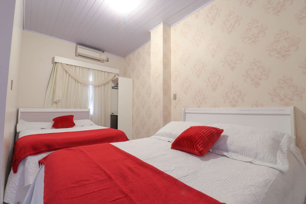 Une chambre d’hôtel avec deux lits, chacun recouvert d’une couverture et doté d’un oreiller rouge, avec des têtes de lit blanches et un miroir au-dessus du lit situé à gauche.