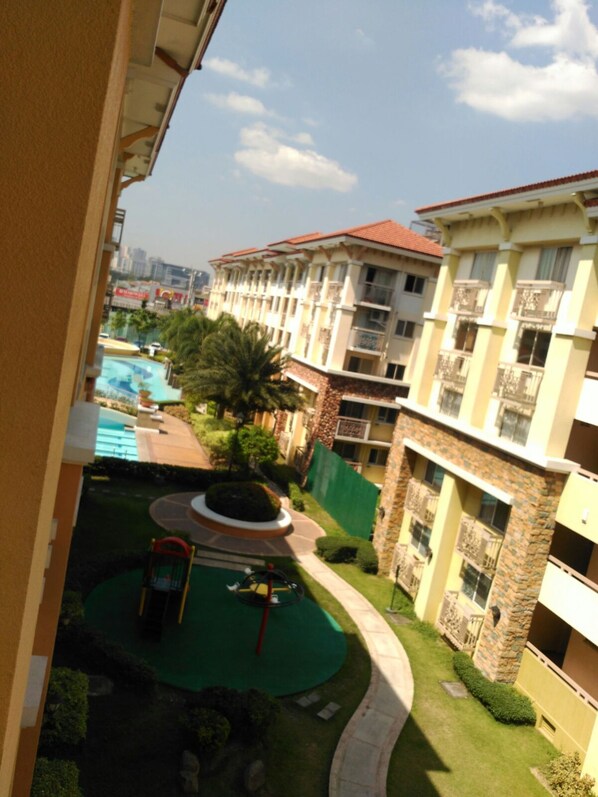 Un hotel de varios pisos con piscina, zona de juegos infantiles y jardín cuidado.