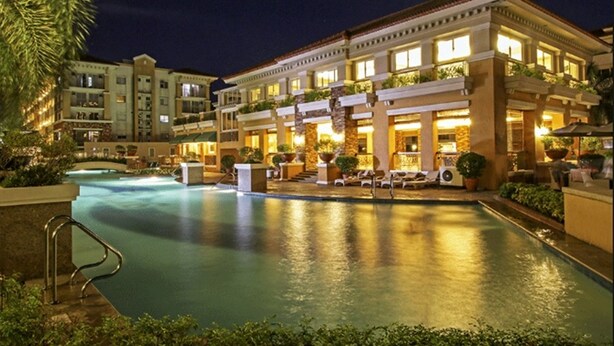 Un hotel con piscina, mobiliario exterior y fachada bien iluminada.