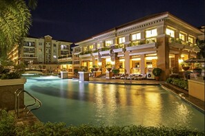Un hotel con piscina, mobiliario exterior y fachada bien iluminada.