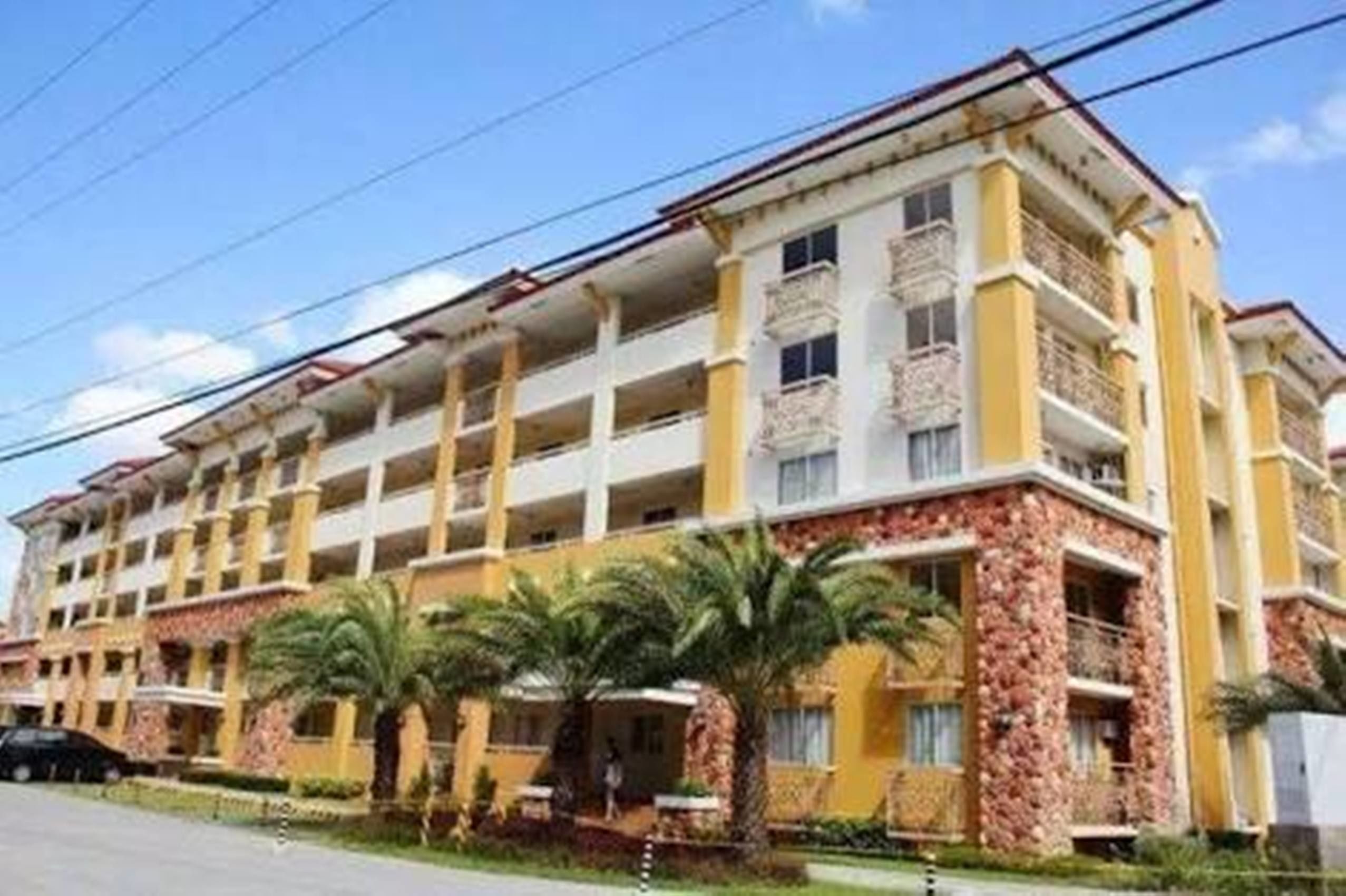 Un hotel de varios pisos con balcones, un patio central con palmeras y un cielo despejado.