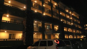 Un hotel de varios pisos con balcones iluminados y un estacionamiento.