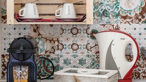 A kitchen counter with a coffee maker, a kettle, and a coffee grinder. There is a shelf above with cups and a decorative vase. - Respiro del Mare (Polignano a Mare)