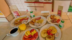 A breakfast table with plates of toast, scrambled eggs, pancakes, and fruit. - Maris B&B (Monteverde)