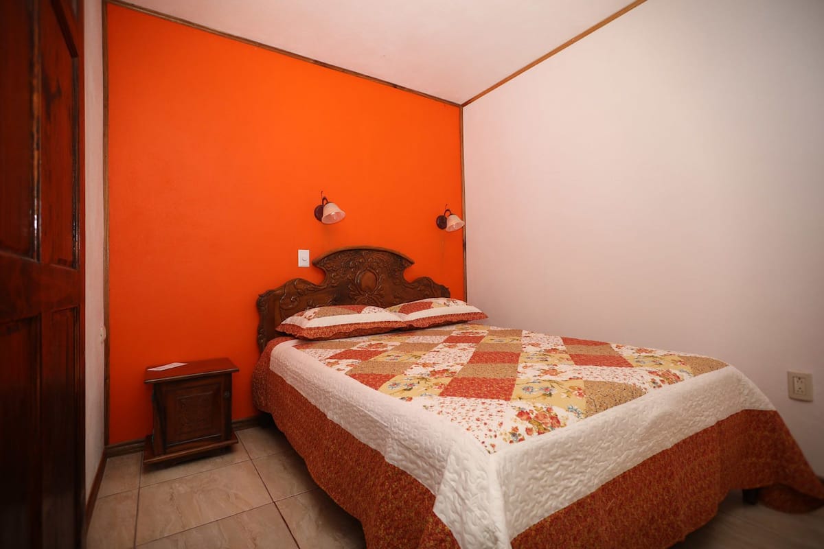 Une chambre avec un lit en bois, un mur orange et un plafond blanc.