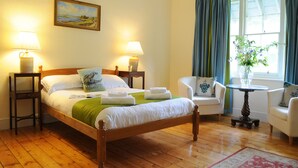 Une chambre à coucher bien rangée, avec un lit en bois, deux tables de chevet avec des lampes, une chaise, une petite table avec un vase et une fenêtre avec des rideaux.