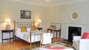 Une chambre à coucher avec un lit à baldaquin, deux tables de chevet avec des lampes, une cheminée, un miroir et un tapis à motifs floraux.