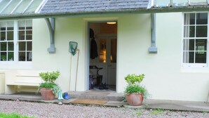 Une maison avec une porte donnant sur une pièce, un banc à l’extérieur et deux plantes en pot sur le porche.