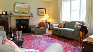 Un salon chaleureux avec une cheminée, deux fauteuils, un canapé et un tapis à motifs.