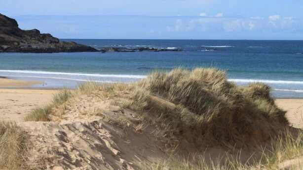 Ein Strand mit Dünen und einer felsigen Küstenlinie.