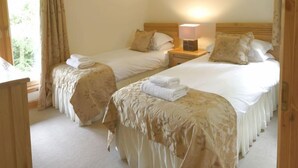 Ein Hotelzimmer mit zwei Einzelbetten, jeweils mit einem Holz-Kopfstück, weißer Bettwäsche und einer Nachttischlampe.