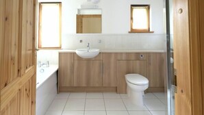 Ein Badezimmer mit einem Holzkosmetikschrank, einem Waschbecken, einer Toilette und zwei Fenstern.