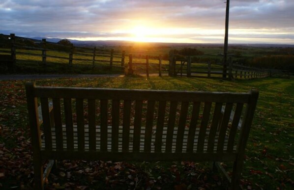A wooden bench in a rural setting with a sunset in the background.